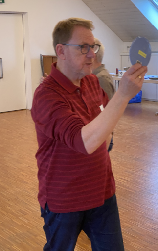 Hans-Ruedi ist von vorn zu sehen, wie er mit ernstem Blick in den Spiegel durch den Raum geht